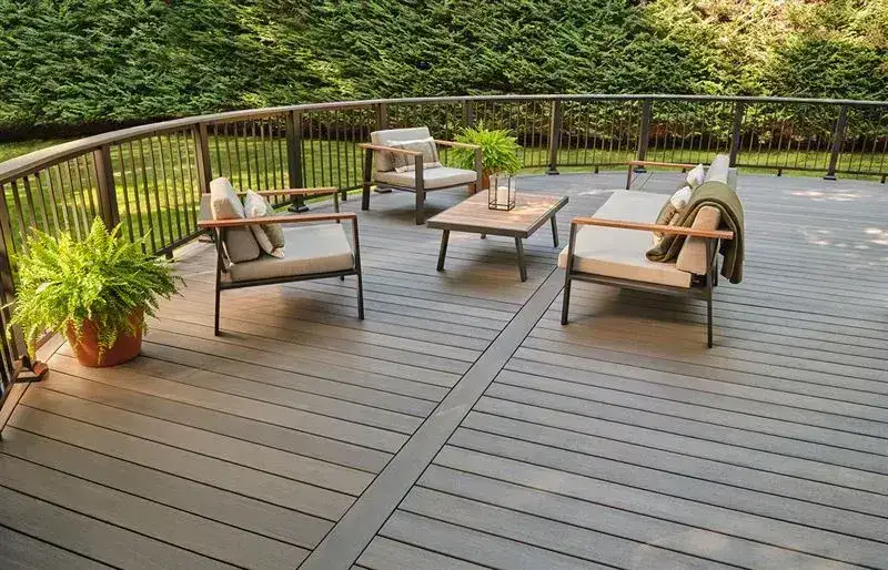 Modern grey composite deck with a curved black metal railing and outdoor patio furniture.