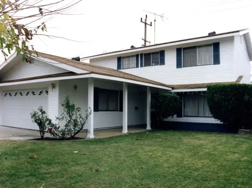 White two-story home featuring horizontal lap siding, blue shutters, a front porch, and attached garage.